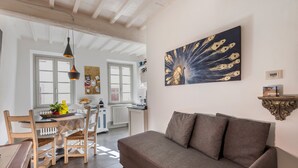 A dining area with a table, chairs, and a sofa. There is a kitchen in the background with a window and a radiator. - GOLD APARTMENT AREZZO CENTER (Arezzo)