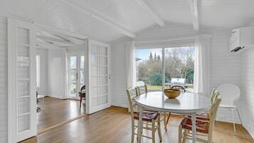 Enjoy meals at the large dining table surrounded by four chairs, with a view of the outdoors through large windows.