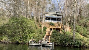 A house with a dock extending into a lake, surrounded by dense forest.