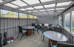 Relax in this stylish outdoor space with metal-framed tables and chairs, surrounded by lush greenery and natural light.