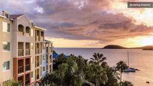 A multi-story building with balconies overlooking a body of water and a sunset in the background.