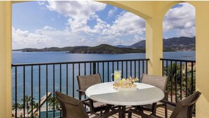 A balcony with a round table and chairs, overlooking a body of water and a mountainous landscape.