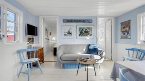 Ein Wohnzimmer mit grauem Sofa, blauen Sesseln, einem Fernseher und Kunstwerken an den Wänden.
