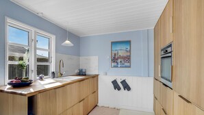 Eine moderne Küche mit Holzschränken, einer weißen Arbeitsplatte, einem Spülbecken und einer hängenden Leuchte.