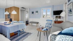 Ein modernes Wohnzimmer mit Essbereich, im Hintergrund eine Küche, ein Sofa, ein Couchtisch und ein Fernseher.