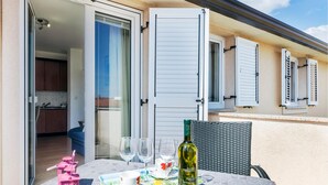 A table set outdoors with a bottle of wine, glasses, and a cup, with a view of a kitchen and sliding doors. - Cozy apartment in Pula with WiFi (Pula)