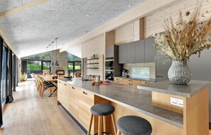 Une cuisine moderne dotée d’un îlot central, de meubles en bois et d’une grande fenêtre offrant une vue sur la verdure.