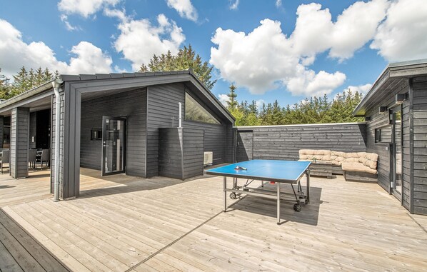 Une terrasse en bois avec une table de ping-pong, des sièges d’extérieur et un espace abrité avec une porte.
