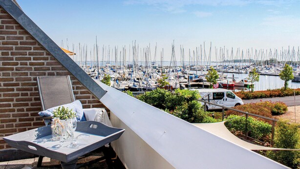 Ein Balkon mit einem Tisch, ein weißer Van und ein Yachthafen mit zahlreichen Booten im Hintergrund.