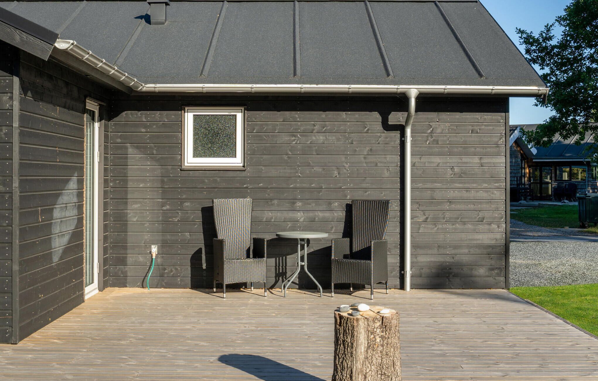 A wooden deck with outdoor seating, a metal railing, and a tree stump.