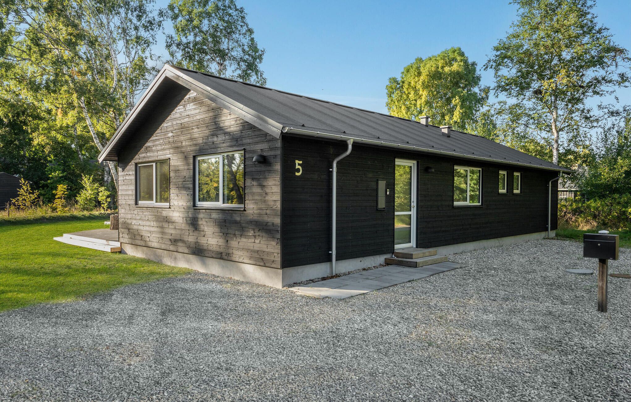 Un bâtiment moderne, de plain-pied, avec une façade sombre, portant le numéro 5, doté de grandes fenêtres et d’une allée gravillonnée.
