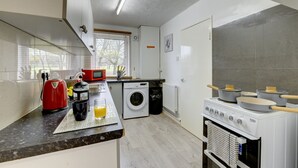 Une cuisine compacte équipée d’un lave-linge, d’une bouilloire rouge et d’une cuisinière.