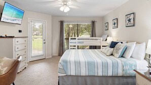 Un dormitorio con cama, escritorio, silla, ventilador de techo y vistas al exterior a través de un ventanal corredera.