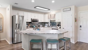 Una cocina moderna con armarios blancos, electrodomésticos de acero inoxidable, una isla de mármol con taburetes y un letrero que dice 'beautiful house'.
