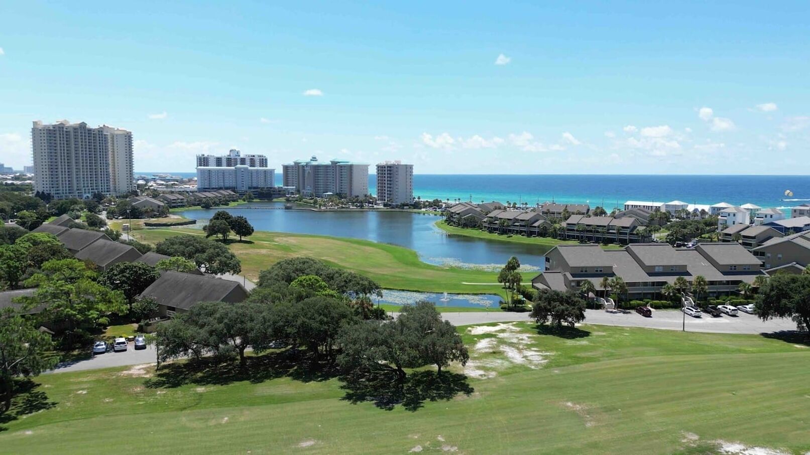 A coastal residential area with multiple high-rise buildings, a golf course, and a body of water.