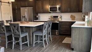 A modern kitchen with dark wood cabinets, stainless steel appliances, and a central island with seating. - Beautiful, newly built 3rd floor Townhouse in historic Elkhart Lake, WI. (Plymouth)