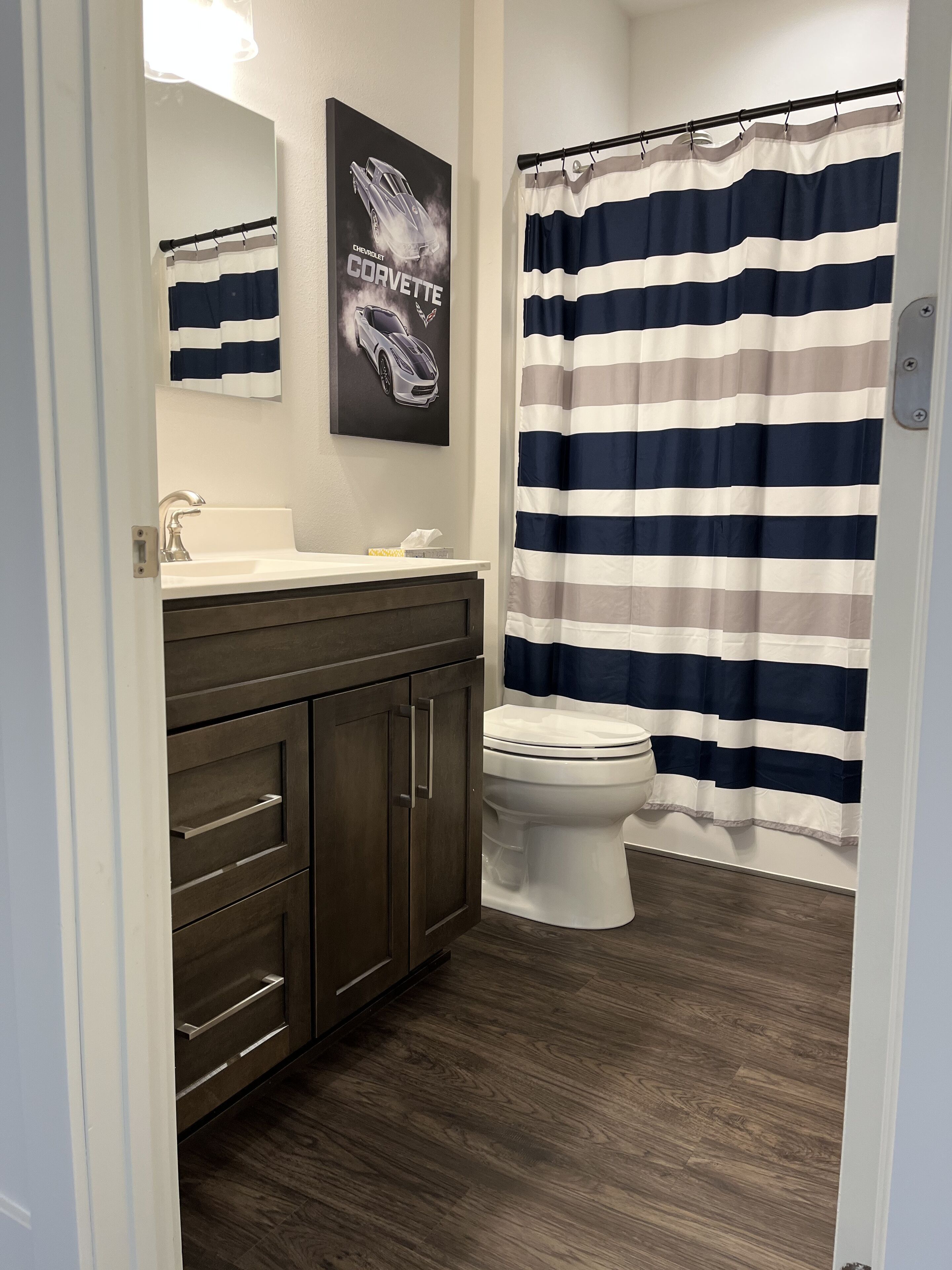 A bathroom with a dark wood vanity, a white toilet, and a striped shower curtain.