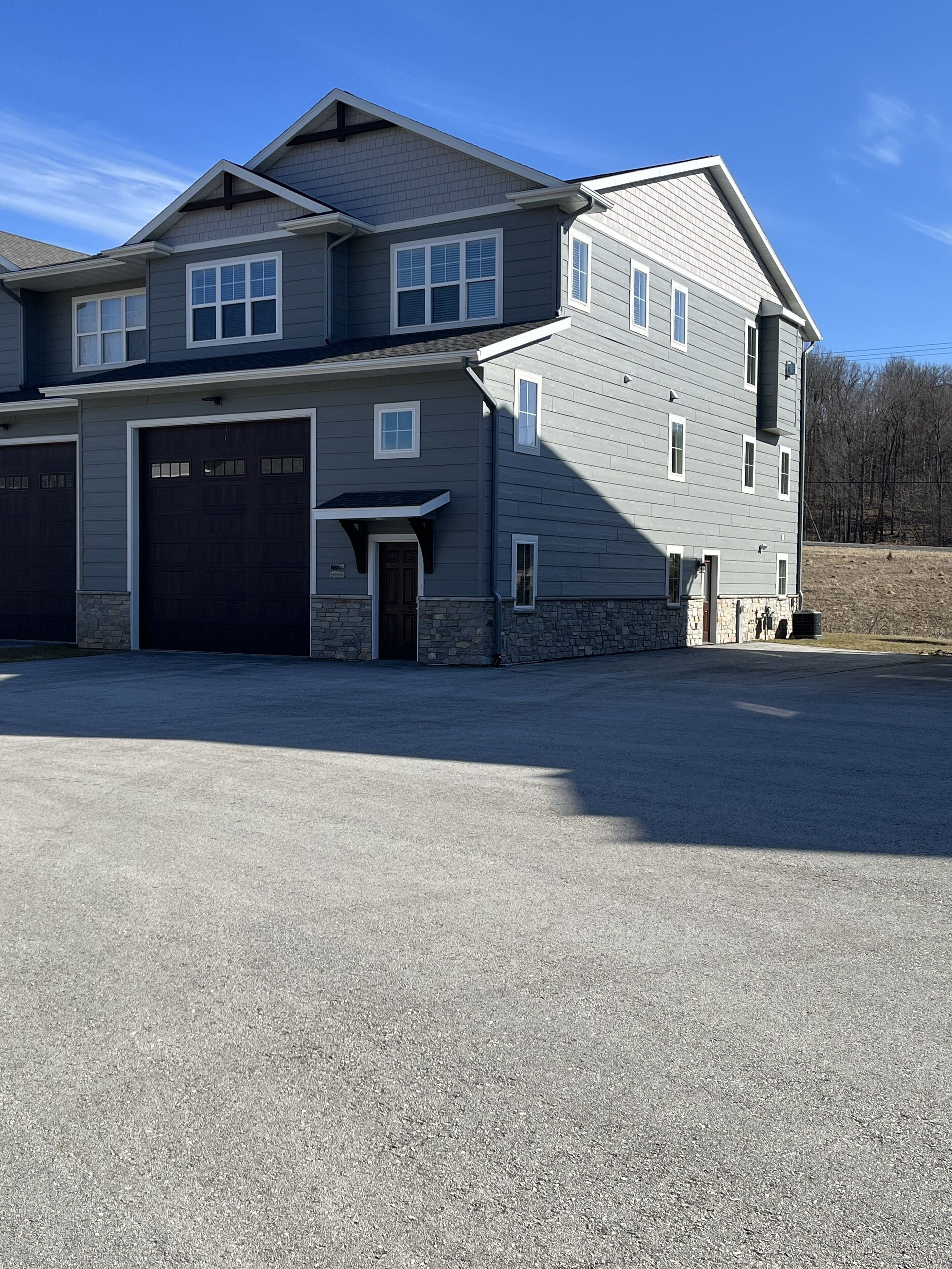 Une maison à deux étages avec un garage, des fondations en pierre et une allée.