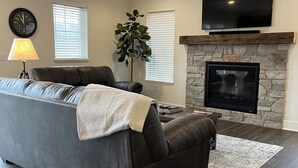 A living room with a gray sofa, a fireplace, a flat-screen TV, and a ceiling fan. - Beautiful, newly built 3rd floor Townhouse in historic Elkhart Lake, WI. (Plymouth)
