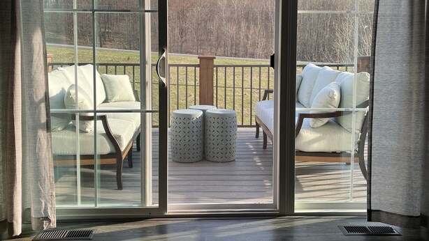 A room with a sliding glass door leading to an outdoor deck with white cushioned seating and a sign reading "ROAD AMERICA ELKHART LAKE". - Beautiful, newly built 3rd floor Townhouse in historic Elkhart Lake, WI. (Plymouth)