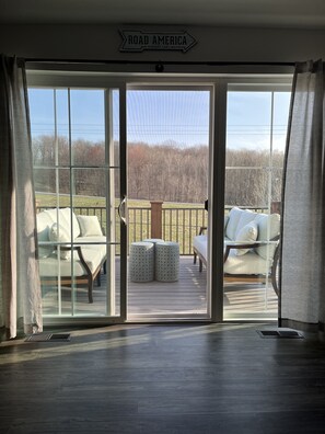 Una habitación con puerta de vidrio corredera que da a una terraza exterior con asientos blancos acolchados y un letrero que dice "ROAD AMERICA ELKHART LAKE".