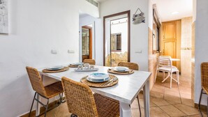 A dining area with a white table set for four, surrounded by wicker chairs. A mirror reflects the room, and a wooden door leads to another space. - Gorgeous home in Marbella with kitchen (Marbella)