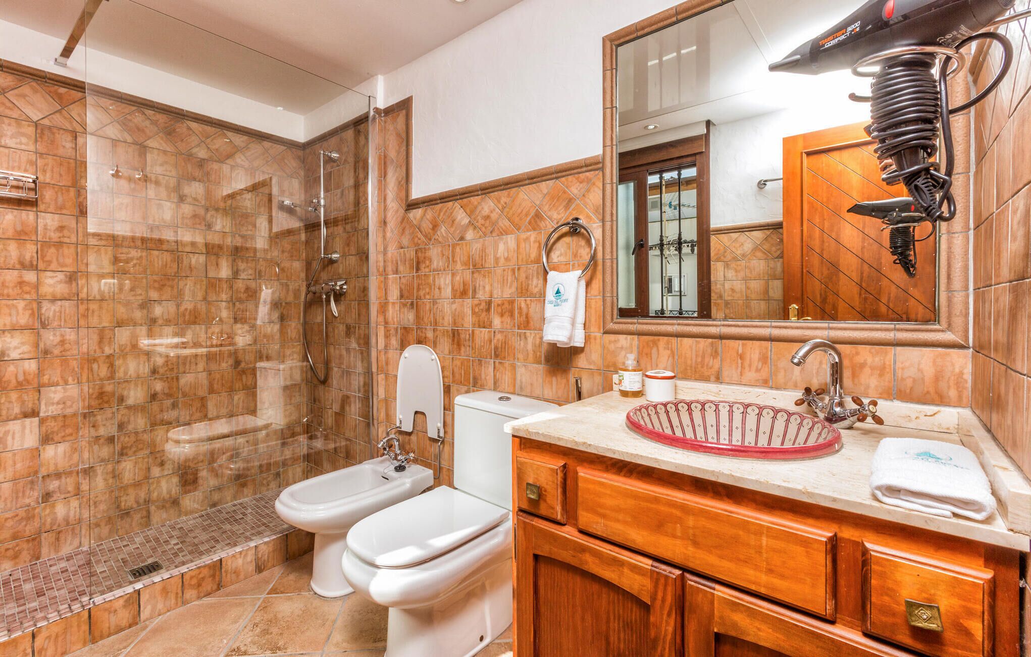 Un baño con ducha, dos inodoros, lavabo y espejo.