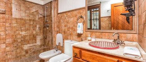 Un baño con ducha, dos inodoros, lavabo y espejo.