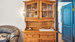 Un armario de madera con puertas de cristal que contiene utensilios de cocina, una cesta de mimbre y una bandeja con un pastel.