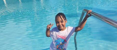 Niño de pie al borde de una piscina con una escalera de metal.