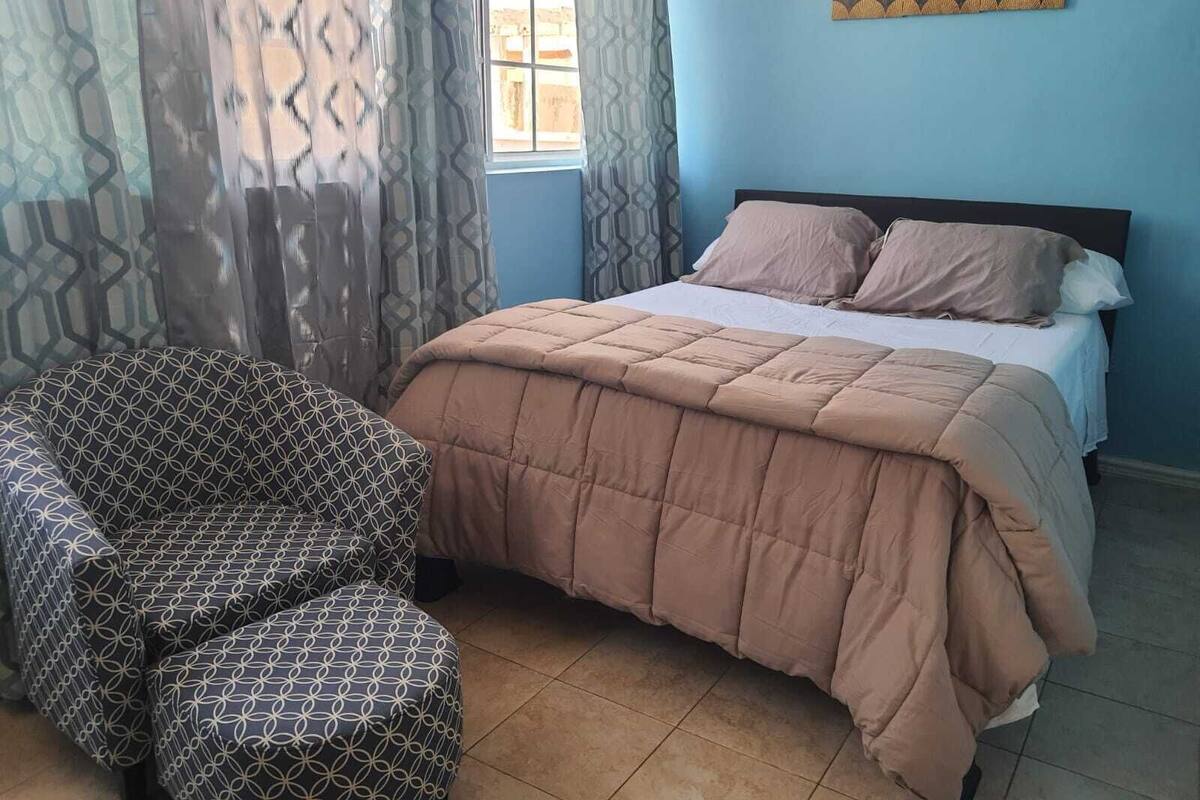 A bedroom with a bed, a patterned armchair, and a window with curtains.