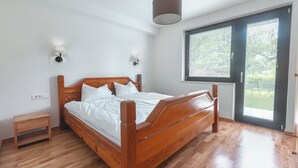 A bedroom with a wooden bed, a nightstand, a wall-mounted lamp, and a window with blinds. - Charming Alpine Retreat – Just Minutes from Lake Bled and Lake Bohinj (Žirovnica)