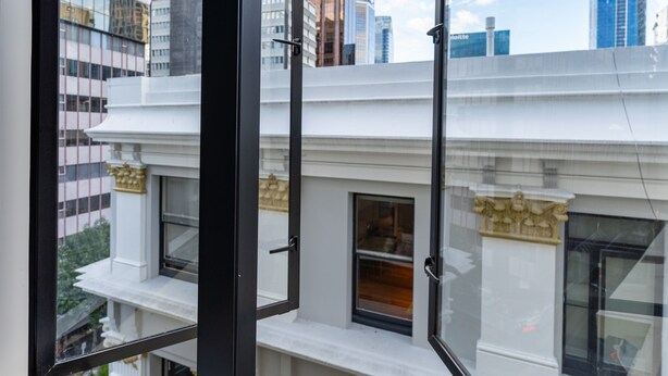 Vista pela janela de um edifício com arquitetura clássica, apresentando uma varanda e uma porta.
