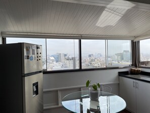 A modern kitchen with a large window, a stainless steel refrigerator, a glass table, and a potted plant. - Studio (Miraflores)