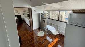 A compact kitchen with a refrigerator, a water dispenser, and a dining area with a glass table and metal chairs. - Studio (Miraflores)