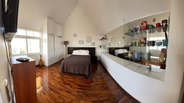 A bedroom with a bed, a desk, a dresser, and a glass display cabinet with decorative items. - Studio (Miraflores)