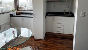 A modern kitchen with white cabinets, a glass dining table, and a view of the city through large windows. - Studio (Miraflores)