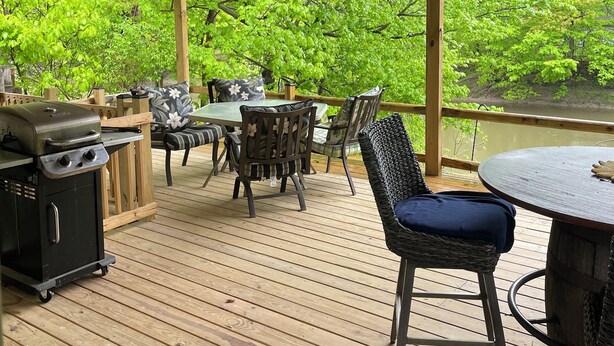 Une terrasse extérieure couverte, dotée d’un plafond en bois, d’un barbecue et d’une table avec des chaises.