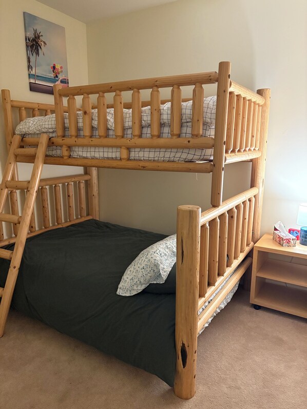 A bunk bed with a wooden frame, a dark green mattress, and a white pillow with a floral pattern.