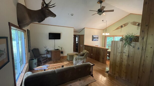 A spacious living room with a large wooden bench, a mounted deer head, a ceiling fan, and a TV on the wall. - Quiet place to land near Lake Michigan, Crystal Lake, Trails, Fishing, and more! (Frankfort)