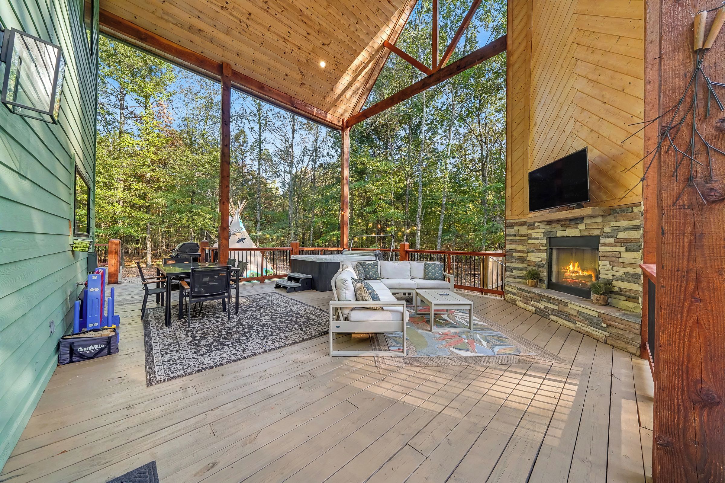 Une terrasse couverte, aménagée avec du mobilier d’extérieur, une cheminée en pierre et une vue sur la forêt environnante.