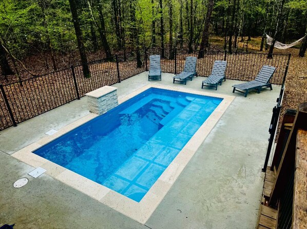 A rectangular swimming pool with a concrete deck, surrounded by a black metal fence.