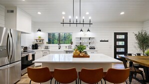 Una cocina moderna con una isla grande, electrodomésticos de acero inoxidable y un comedor con mesas y sillas de madera.