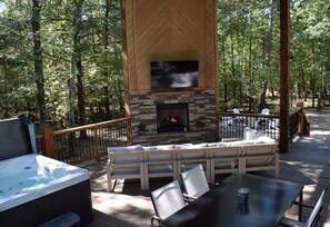 A deck with a stone fireplace, outdoor seating, and a hot tub.