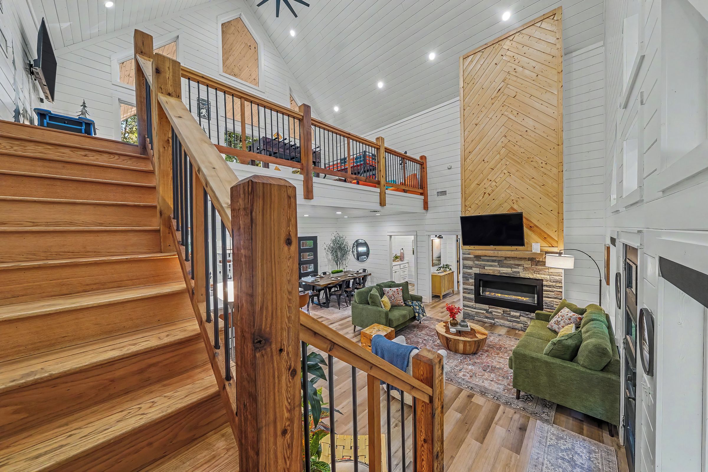 A spacious living area with a wooden staircase, a fireplace, and a high ceiling with exposed beams.