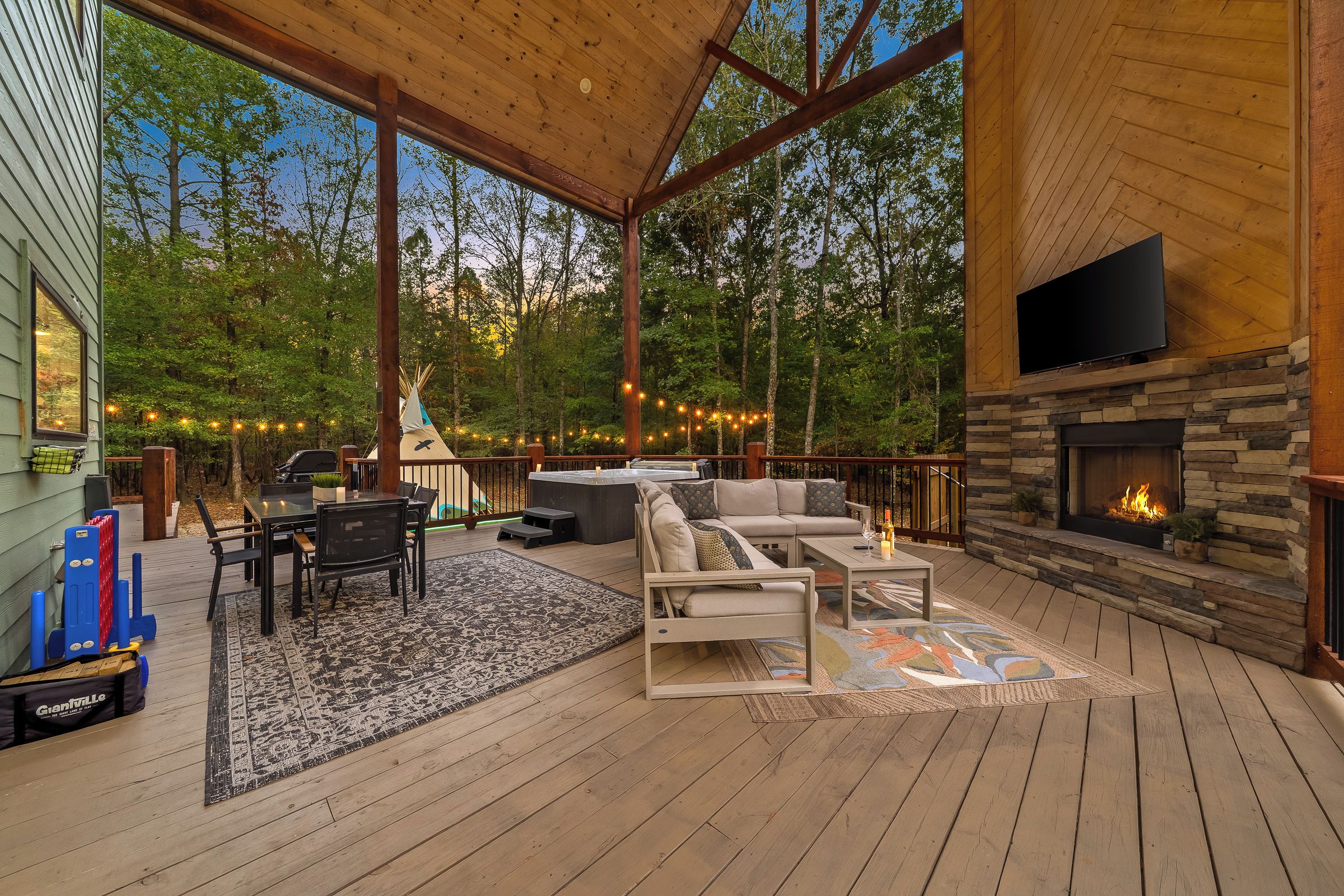 A wooden deck with a stone fireplace, outdoor seating, and a view of the forest.