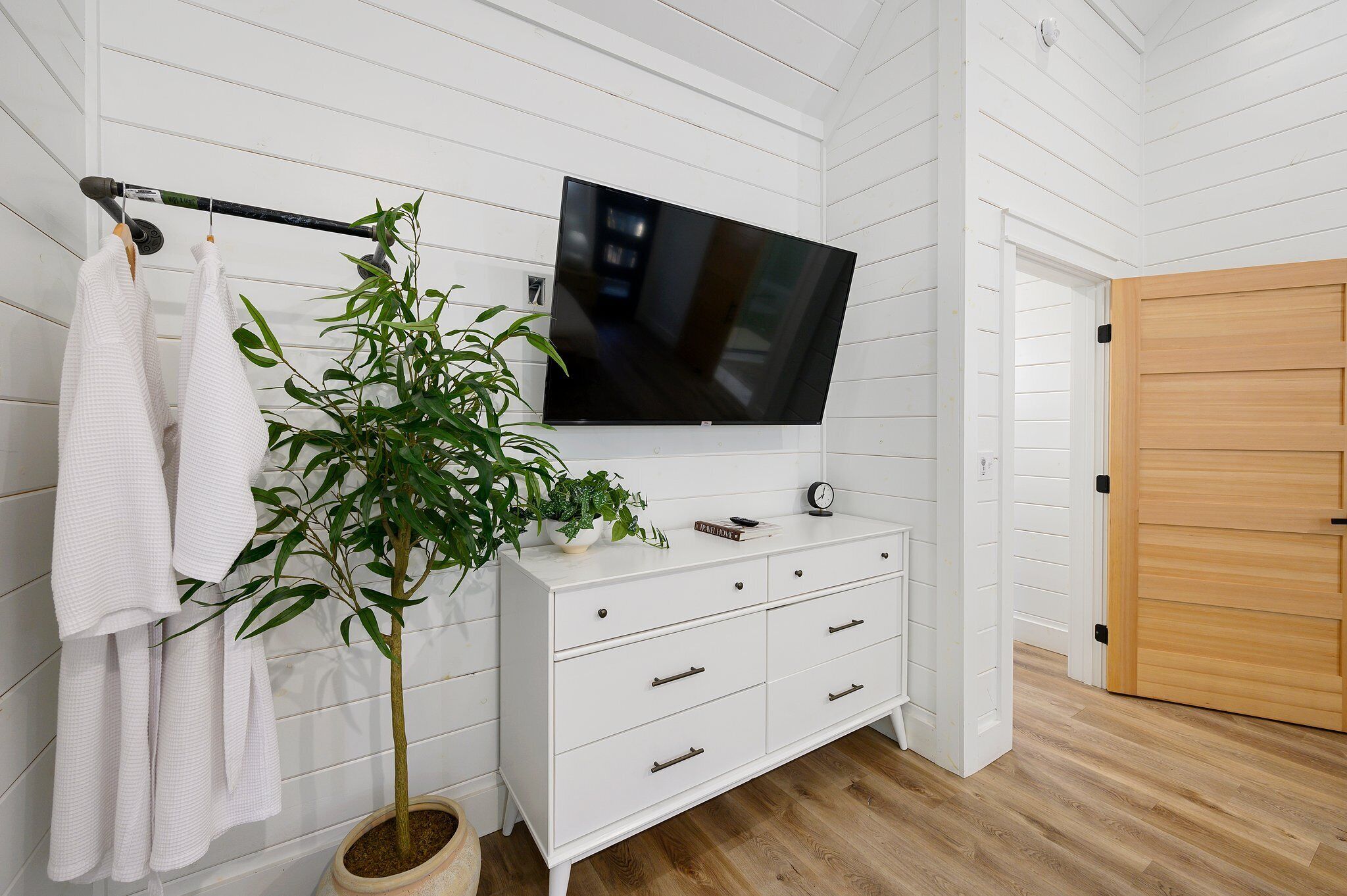 A bathroom with a white vanity, a potted plant, a hanging towel, and a mounted television.