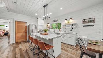 A modern kitchen with white cabinetry, a central island, and a dining area with a wooden table and chairs.