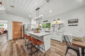 A modern kitchen with white cabinetry, a central island, and a dining area with a wooden table and chairs.