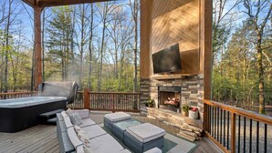Una terraza de madera con mobiliario exterior, un jacuzzi y una chimenea de piedra.